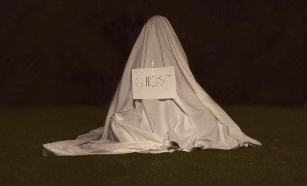 A person wearing a sheet over their head with a sign reading "ghost" in front of them
