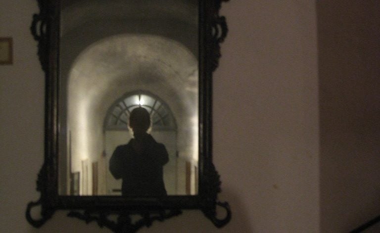 A dark figure reflected in a mirror