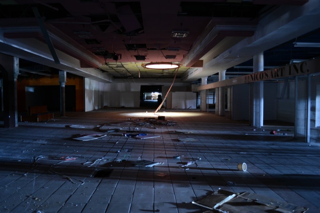 the interior of a dead shopping mall, dark, abandoned, and falling apart
