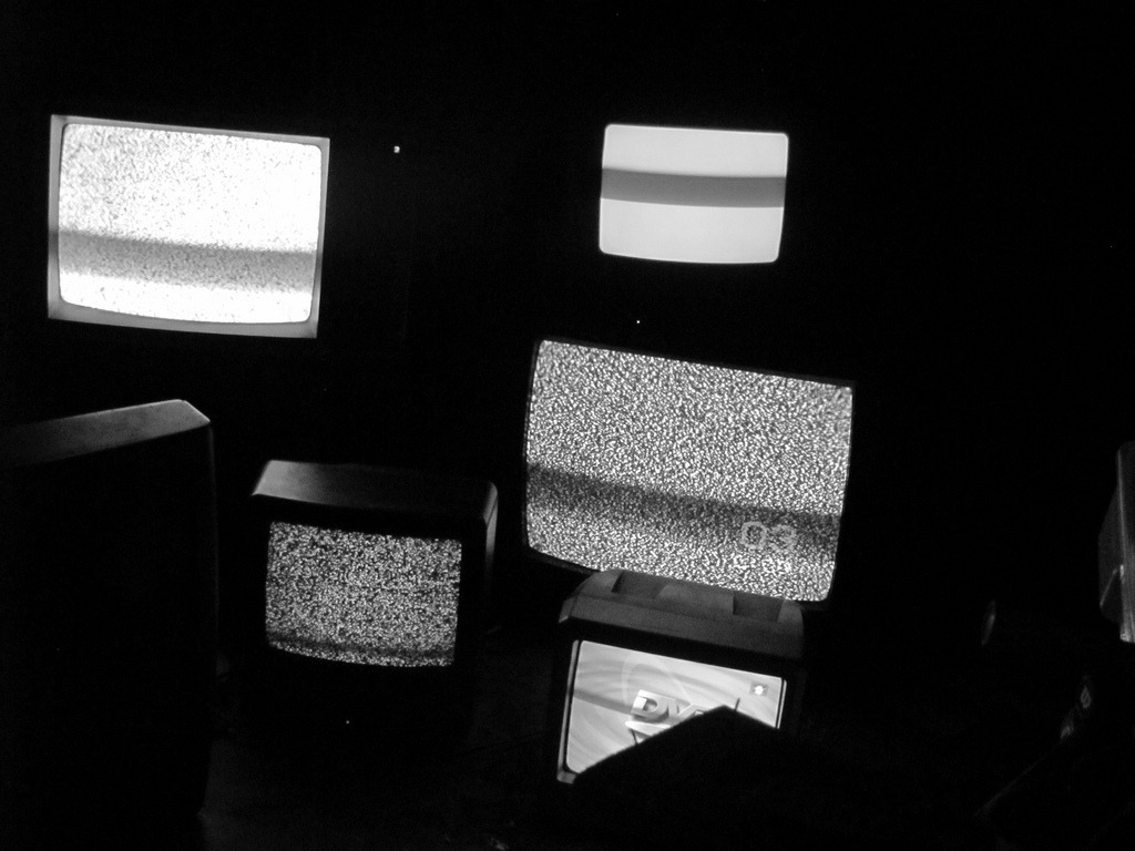 A bunch of televisions in the dark, all showing static on their screens