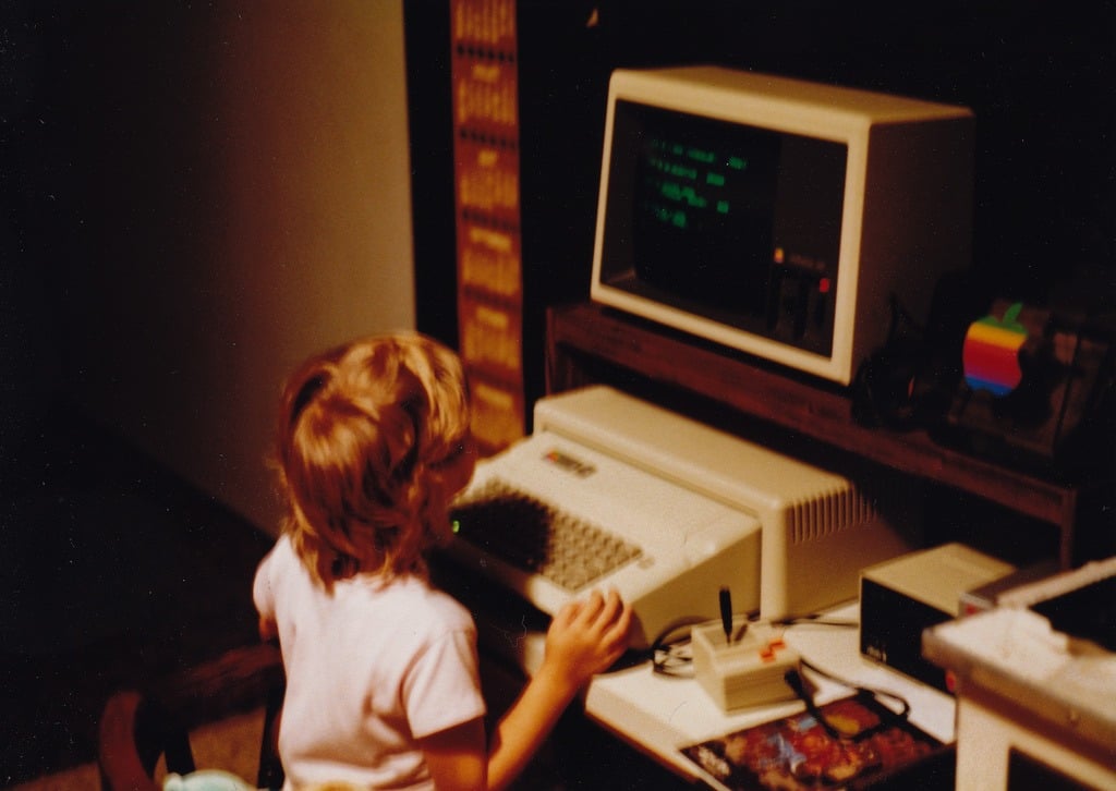 A child sitting at a vintage computer in the 1980s
