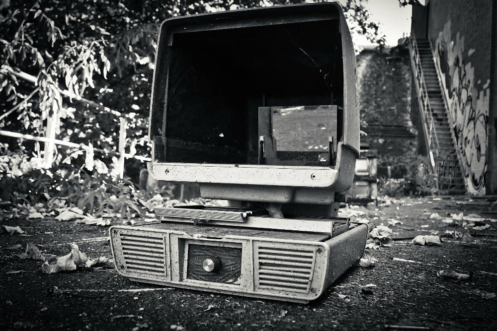 A black and white photograph of a vintage desktop computer sitting abandoned on the ground outside.