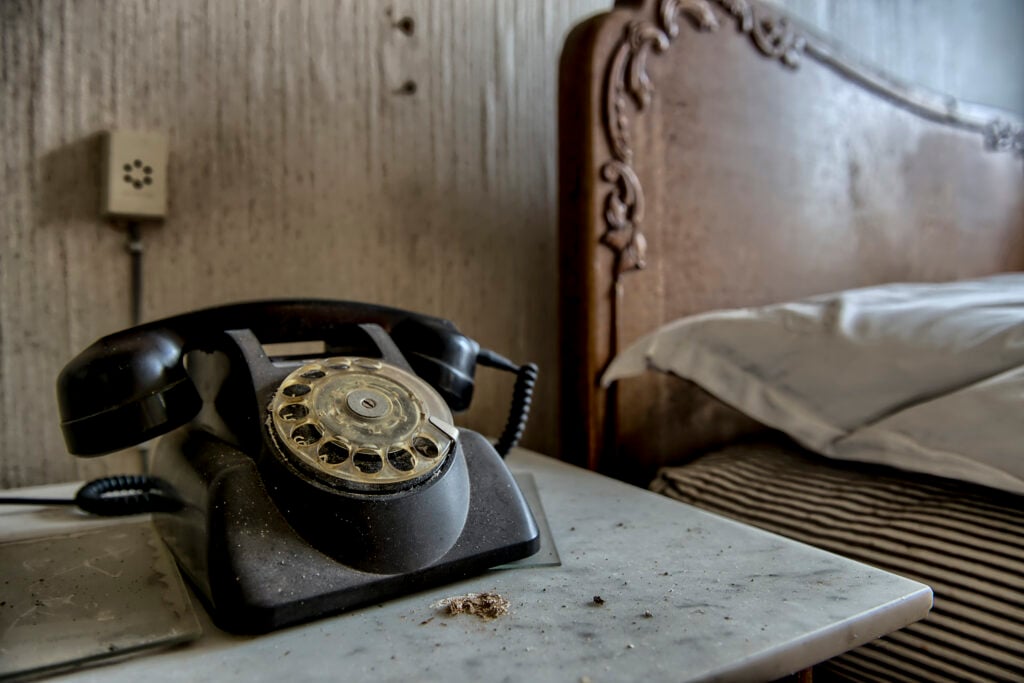 a rotary phone sitting beside a bed in an abandoned bedroom