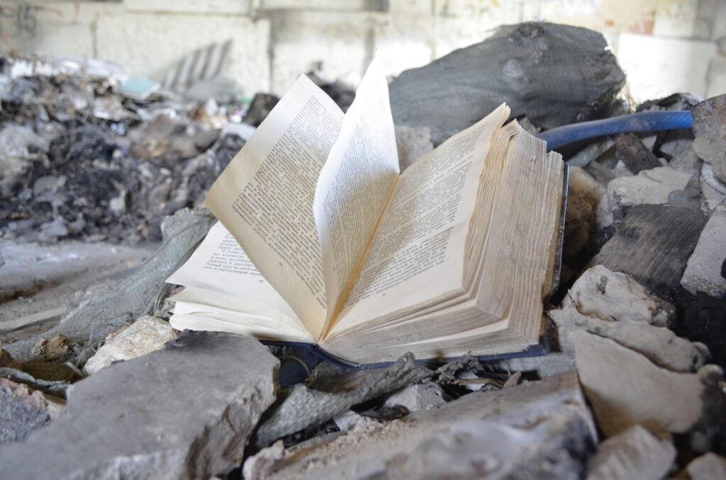 An abandoned book, open, on a pile of rubble, pages flapping.