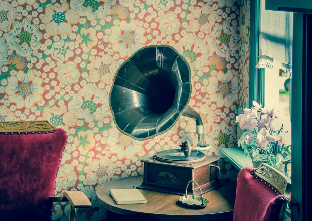 A big, old-fashioned phonograph sitting on a table in a room with lurid, floral wallpaper.