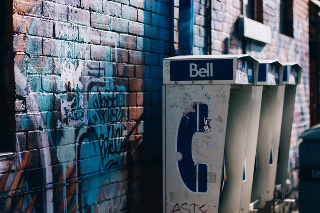 A row of old payphones against a graffiti'd building