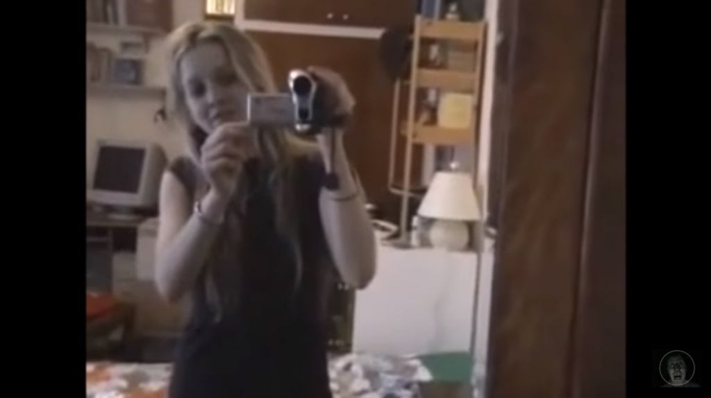A blonde, white, female-presenting person - Louise Paxton - holding her video camera in front of a mirror
