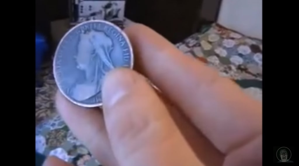 A hand holding a very old coin