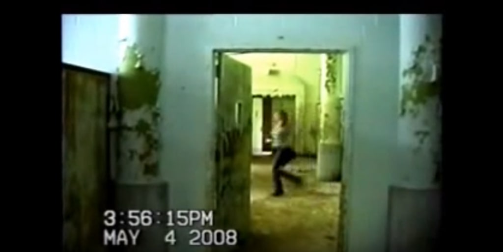 A female-presenting person running from right to left past a doorway in the abandoned ruins of the Pennhurst State School and Hospital