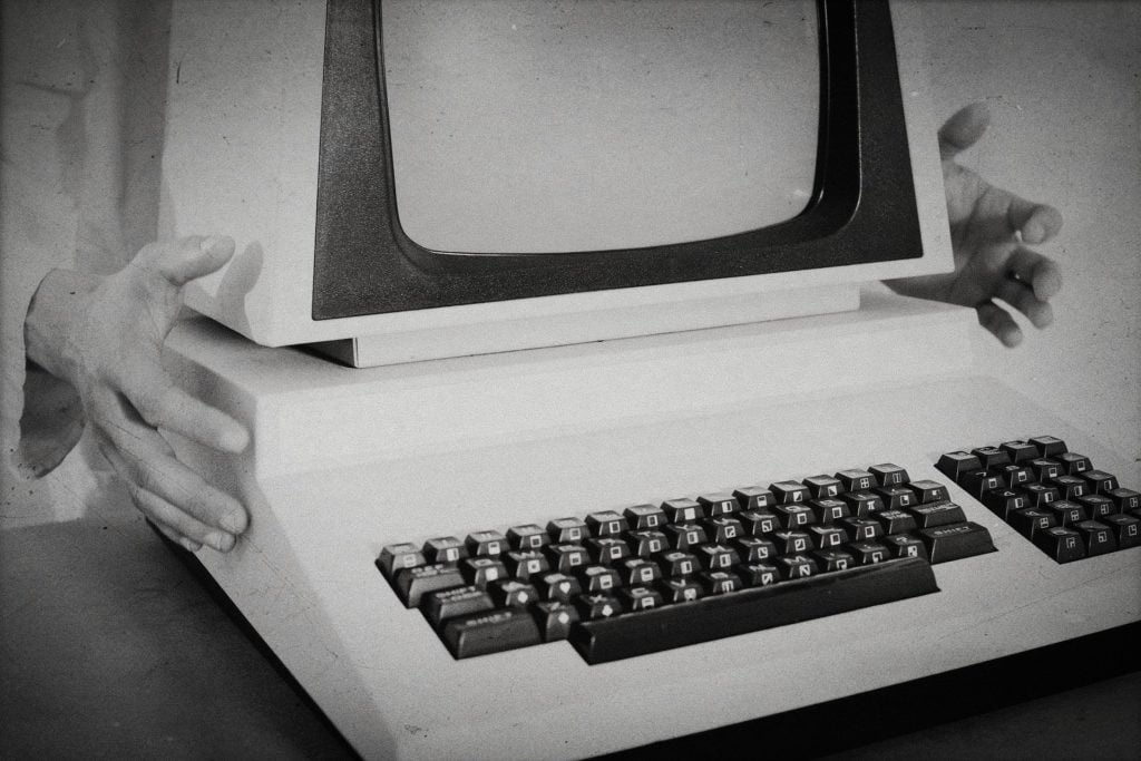 A vintage computer with two hands grasping it from the sides.