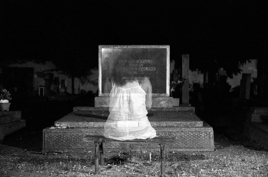 A ghostly girl sitting before a grave stone