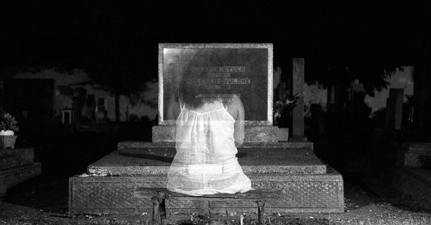 A ghostly girl sitting before a grave stone