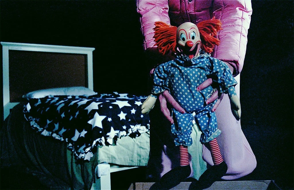 A child in a bedroom with a clown doll