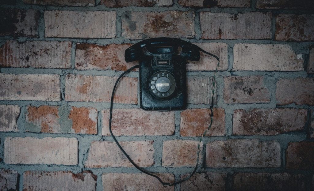 A black rotary telephone hanging on a brick wall