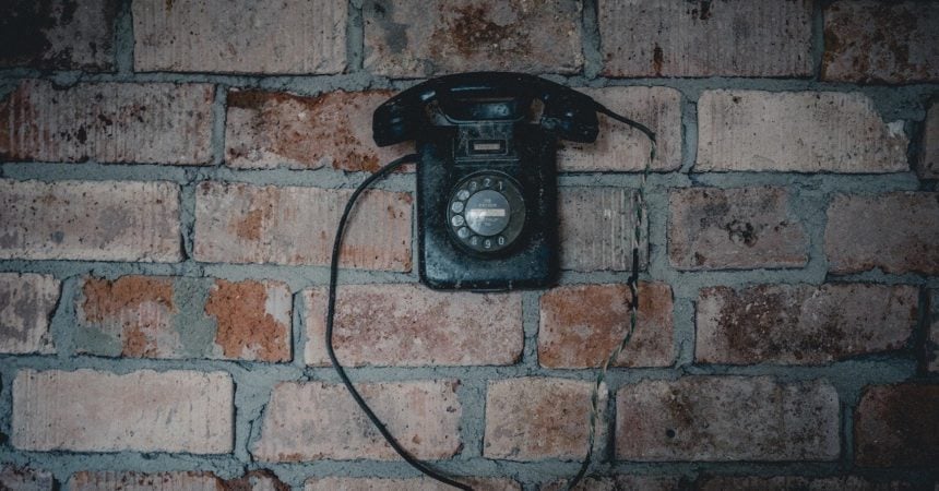 A black rotary telephone hanging on a brick wall