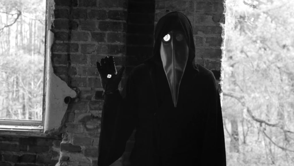 A person in a plague doctor mask standing in an abandoned building