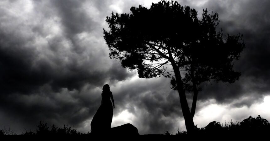 A woman silhouetted against a cloudy sky with a tree next to her