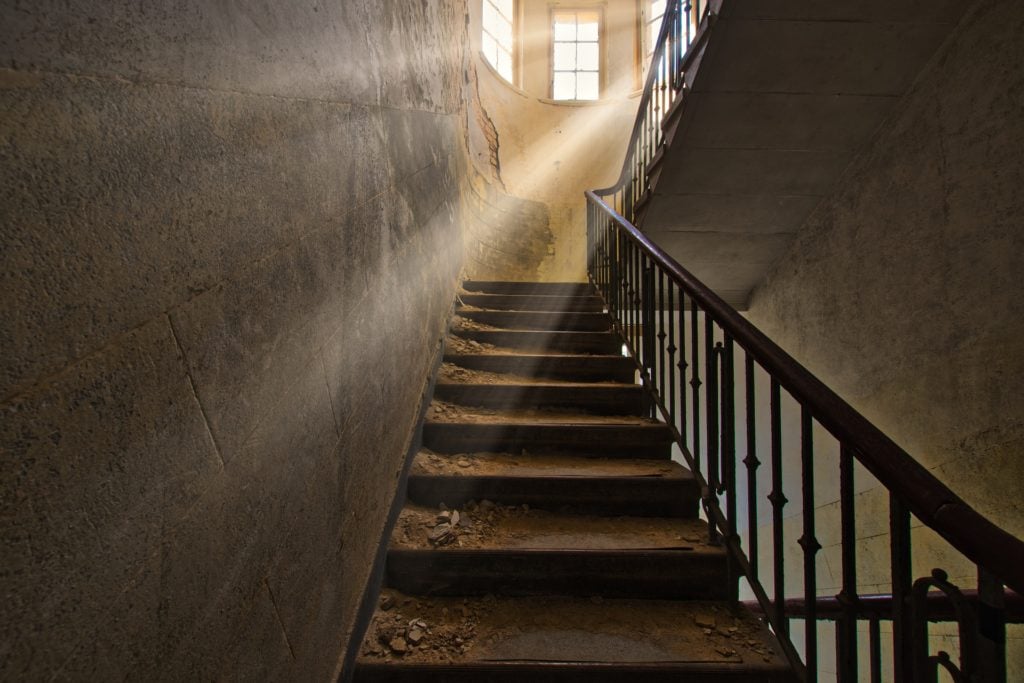 Looking up a dusty staircase in an abandoned building with a window at the top