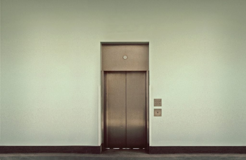 A modern, metal elevator door set in a stark, white wall.