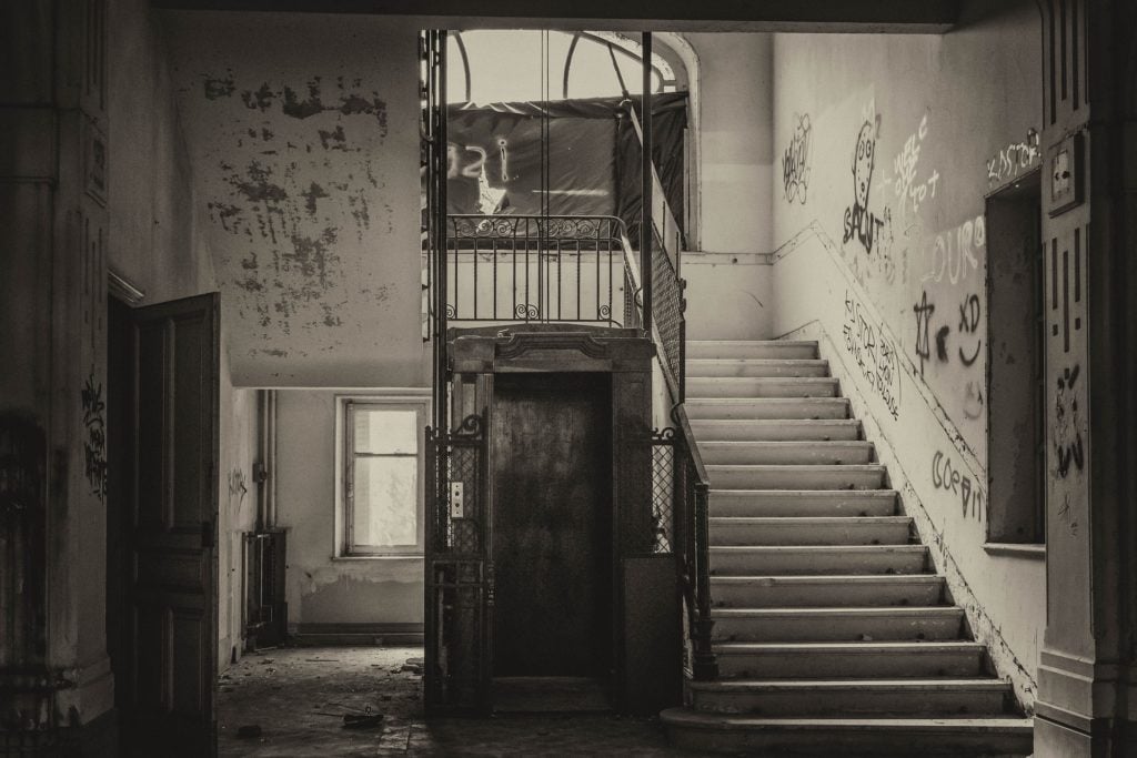 An elevator with a staircase next to it in an abandoned building