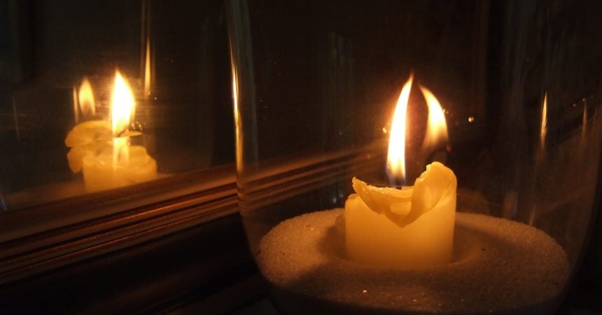 A candle burning in a dark room next to a mirror