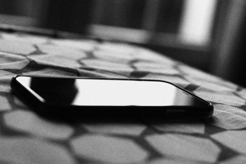 A black and white photo of an iPhone sitting face-up on a honeycomb-patterned surface.