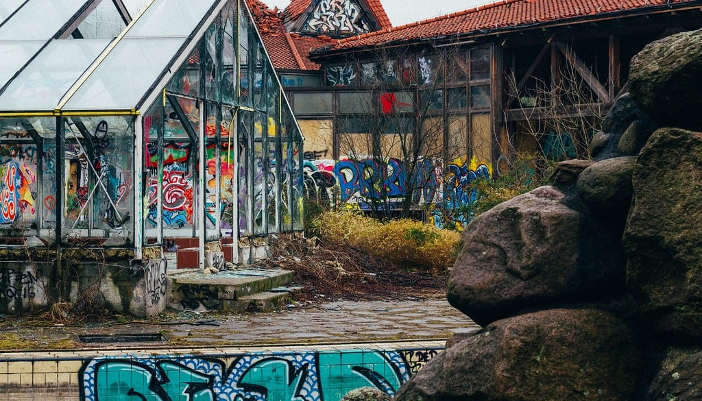 The exterior of a glass building and a red-roofed building covered in graffiti at the abandoned Blub water park in Berlin, 2015.