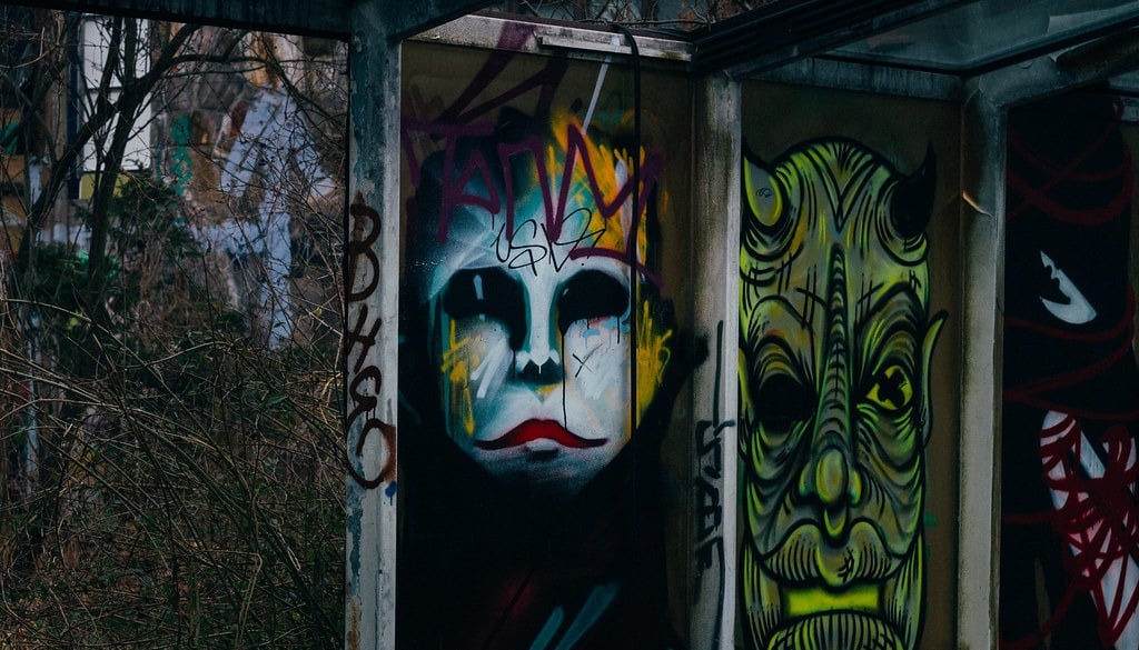 Graffiti on the walls of the abandoned Blub water park in Berlin, 2015: A large, white face with red lips and black eyes; next to it, a large green monster face with horns.