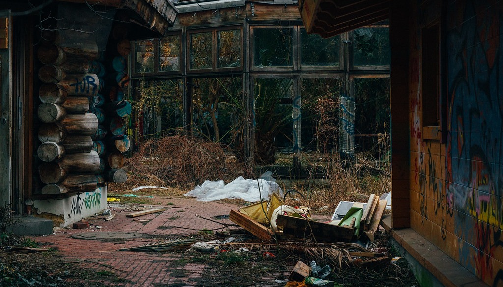 An exterior area of the abandoned Blub water park in Berlin, 2015. There is a log cabin to the left, a wooden building to the right, and a glass building straight ahead.