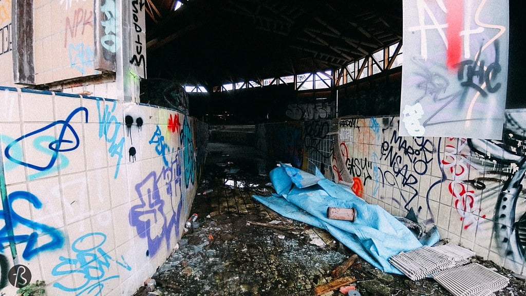 The narrowing walls of an outdoor pool heading indoors at the abandoned Blub water park in Berlin, 2015. There is graffiti on the tile walls. There is no water in the pool.