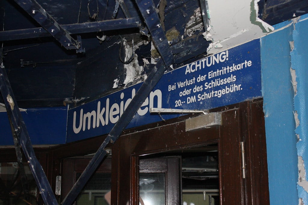 A large blue sign with white writing over a door at the abandoned Blub water park in Berlin, 2015. The sign is German and reads "Umkleiden" and "ACHTUNG!"