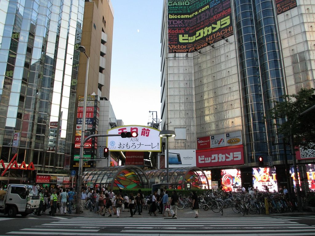 A busy shopping district street surrounded by tall buildings in Namba, Osaka, Japan.