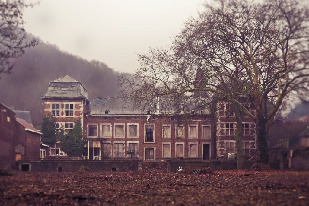 A long, two-story, brick manor house that has been abandoned for some time.