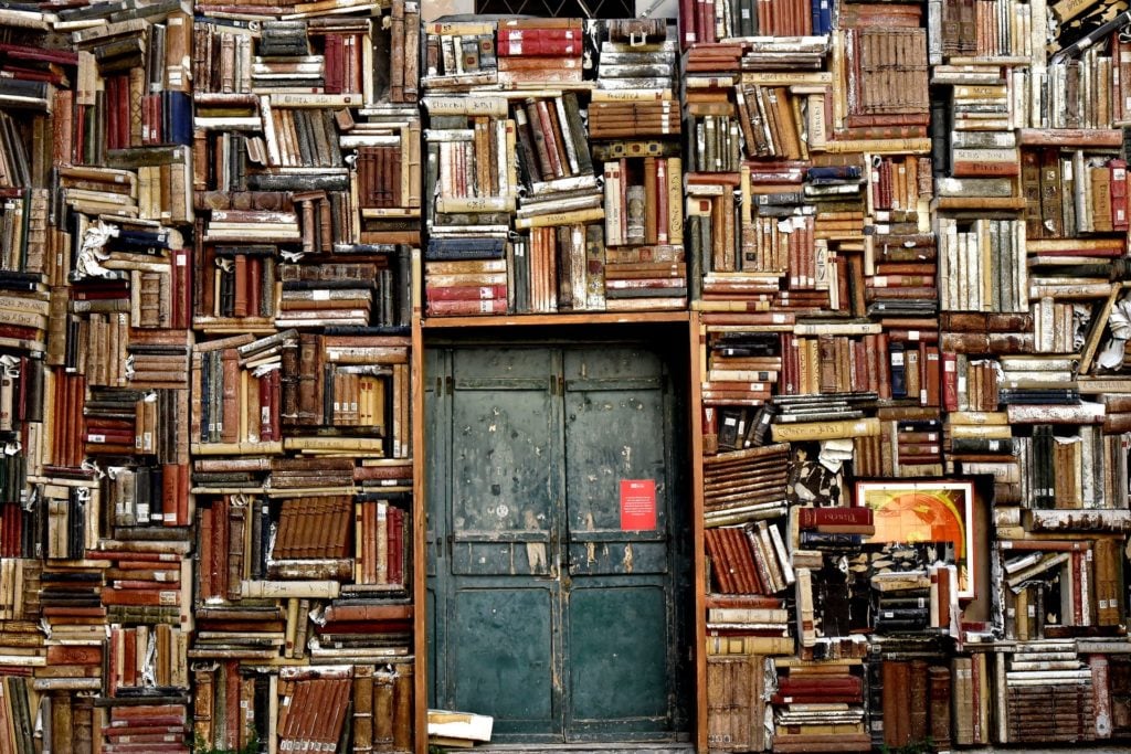 An industrial metal door surrounded by a wall of books shelved every which way.