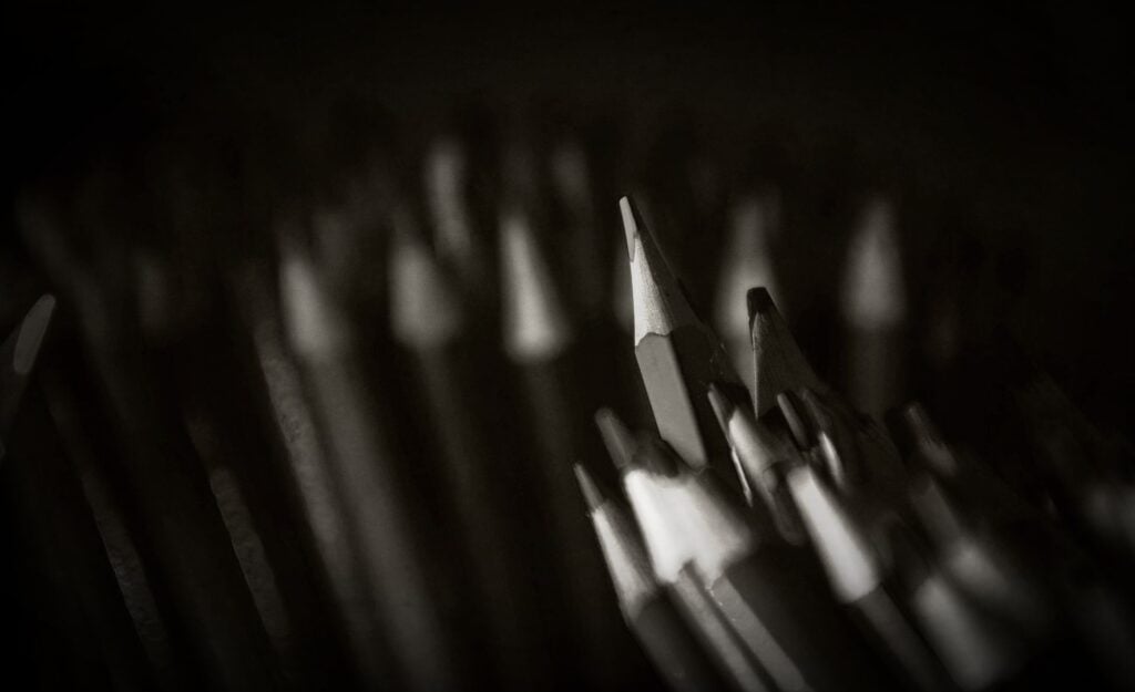 A black and white image of a large collection of wooden pencils, sharpened, standing up in bunches.