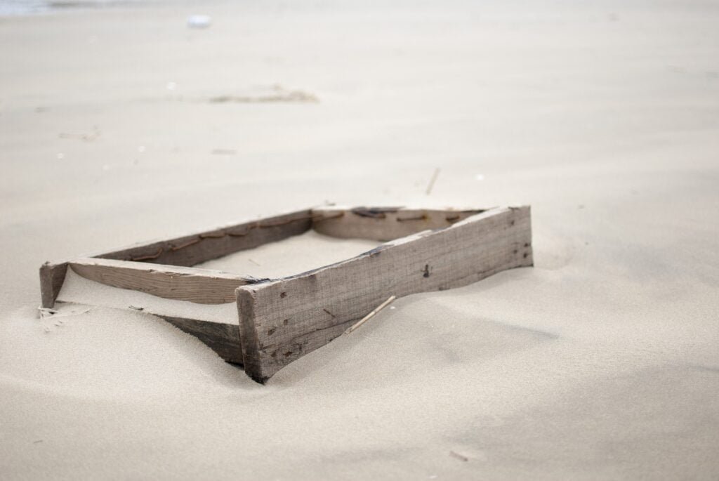 An old, weathered, wooden sandbox sitting in a larger desert of sand.