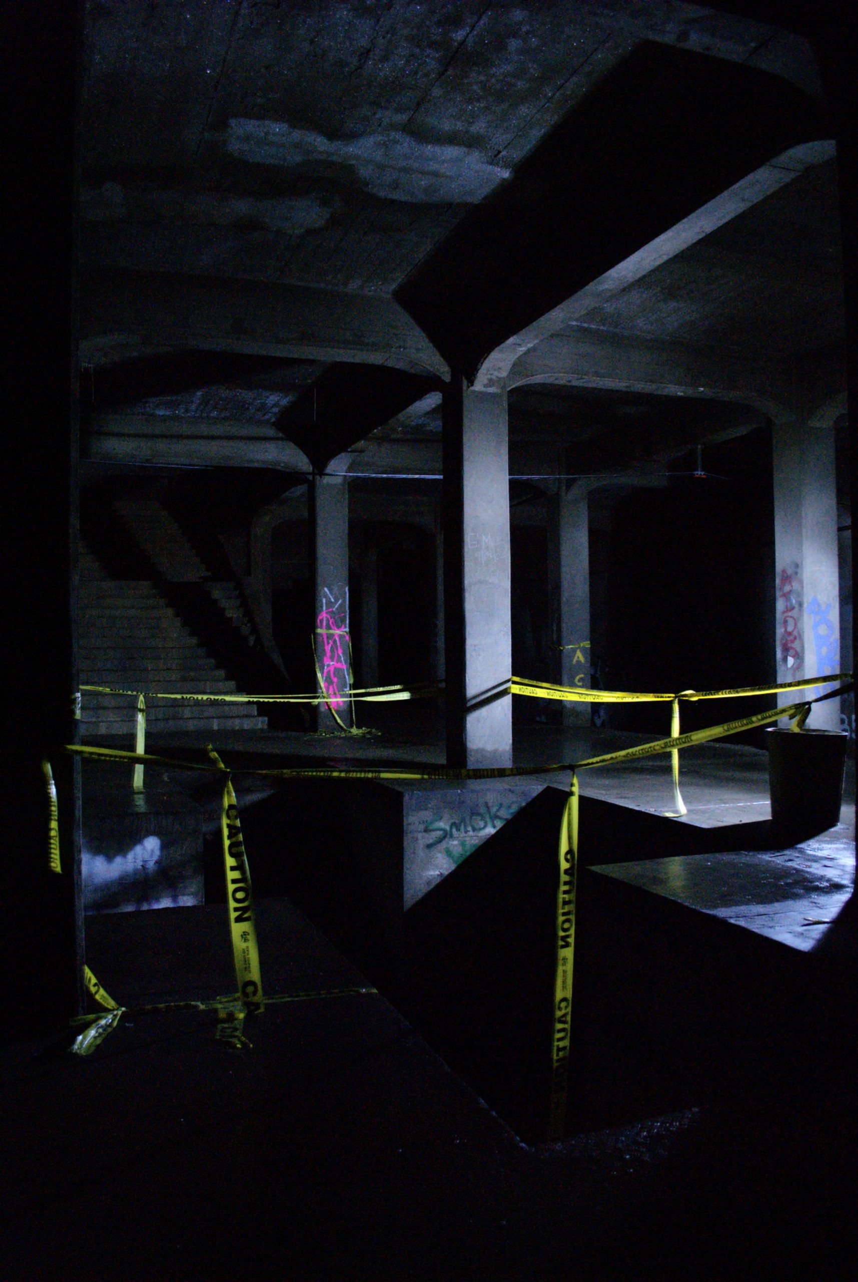 A dark, empty platform wrapped in yellow "Caution" tape in the abandoned Cincinnati Subway.