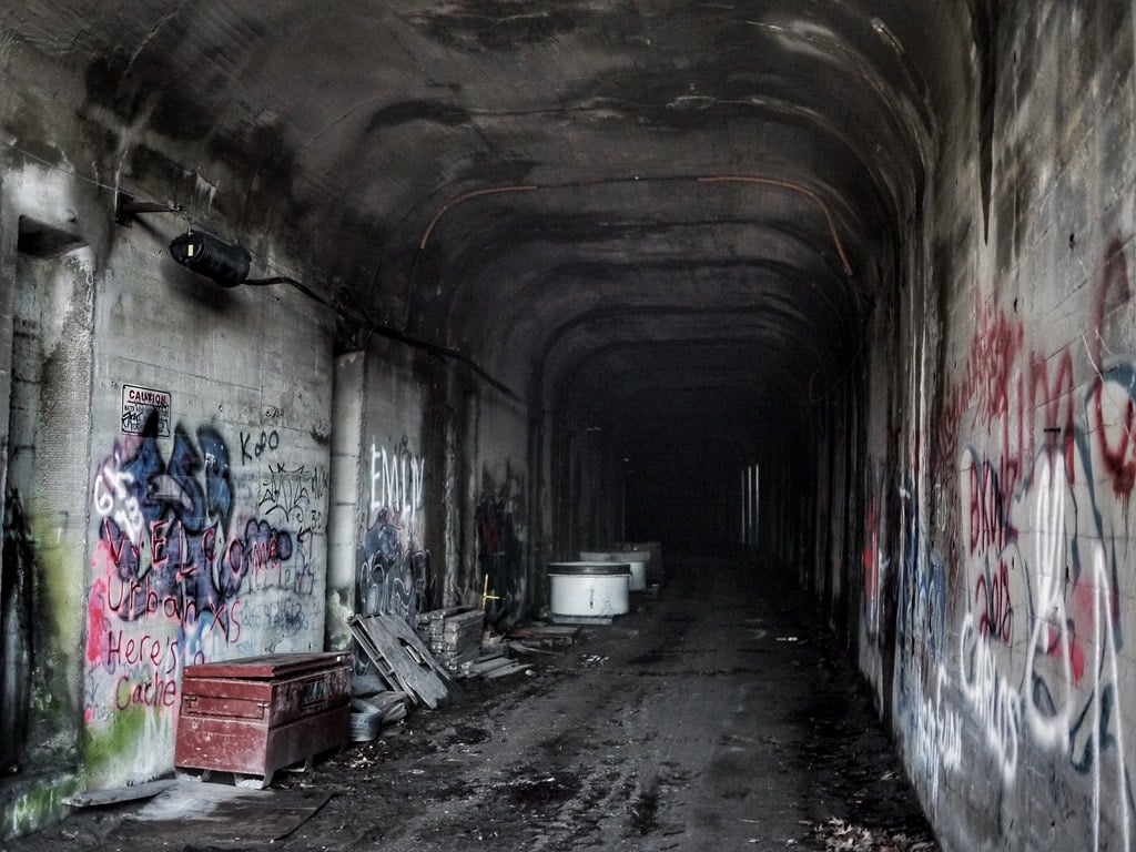 A tunnel within the abandoned Cincinnati Subway. The walls are covered in graffiti and there is debris scattered about.