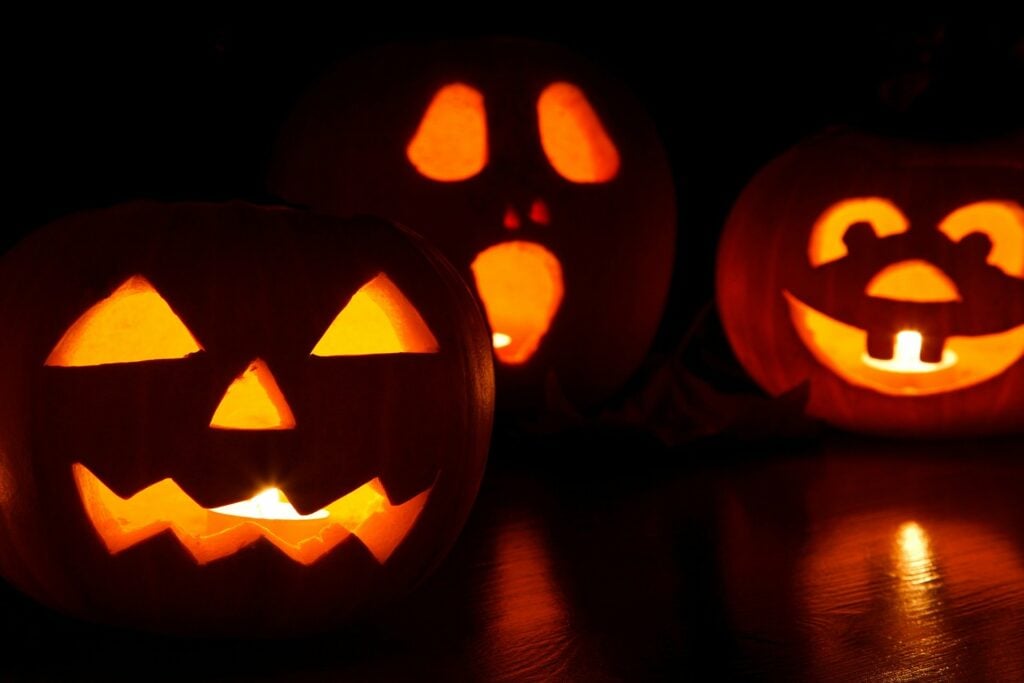 Three carved jack o' lanterns, lit and sitting on a flat surface in an otherwise dark room.