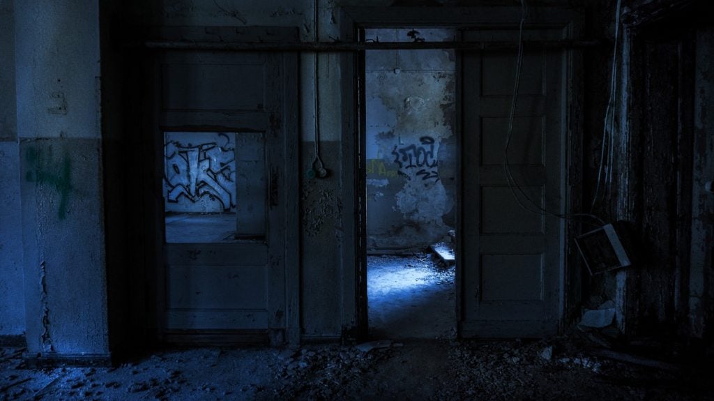An open door in a rundown, abandoned building. The light is dim and blue, and the walls are covered in graffiti.