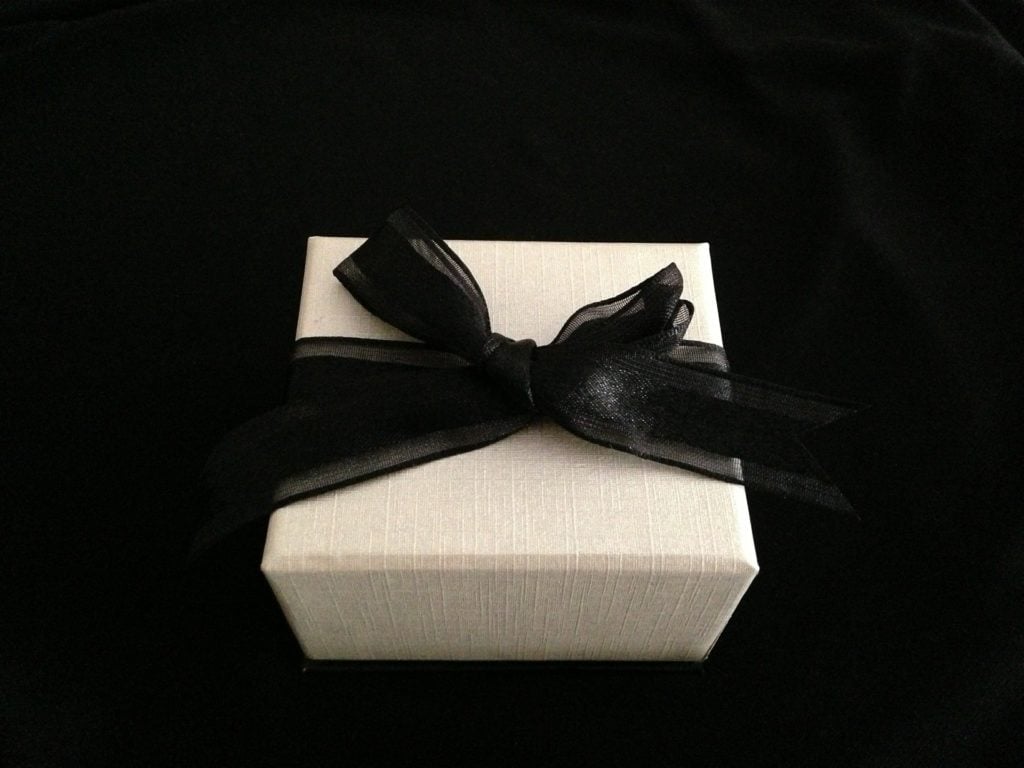 A small, white gift box with a black bow. The box is sitting on a black surface.