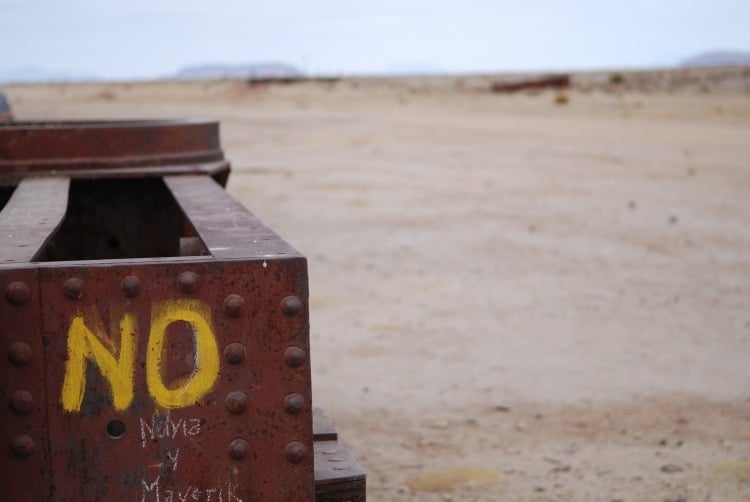 Close-up detailing on a piece of abandoned train car in the desert. Yellow graffiti on it reads, "NO."