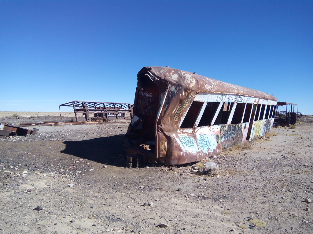 An abandoned, slightly crushed train car with no wheels against a blue sky in the desert.