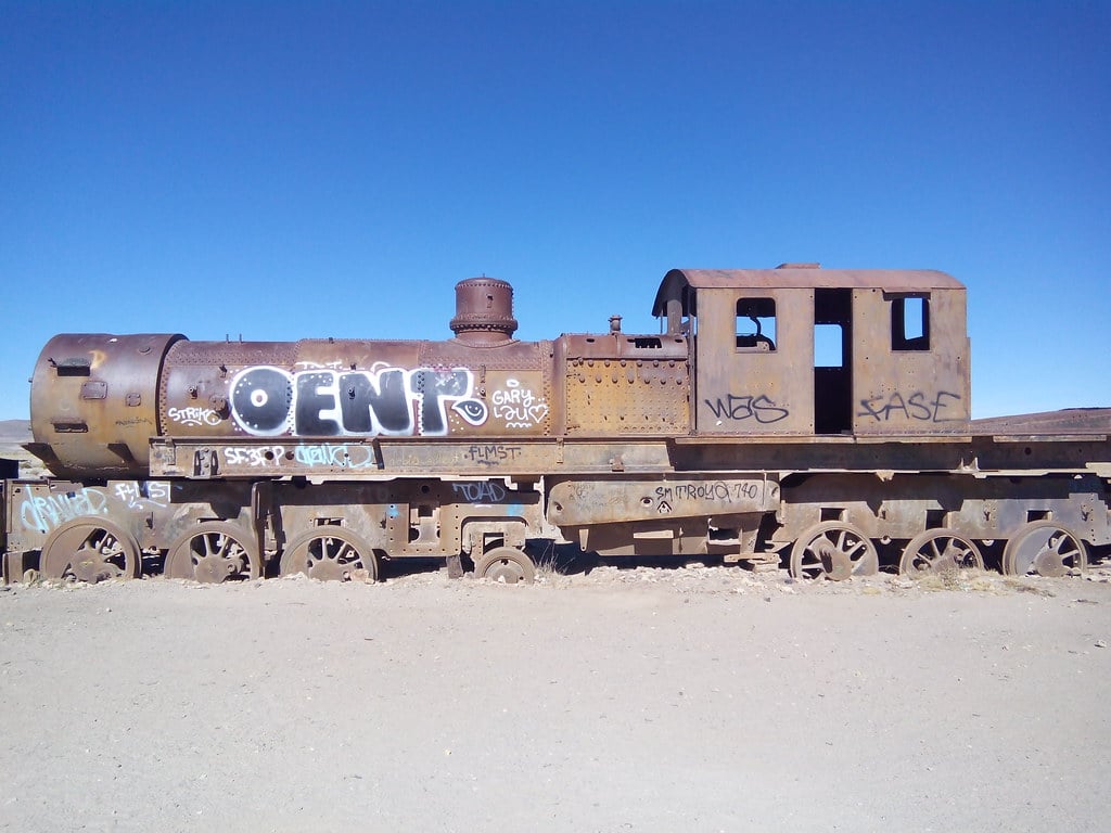 An abandoned train engine covered in graffiti against a blue sky in the desert.
