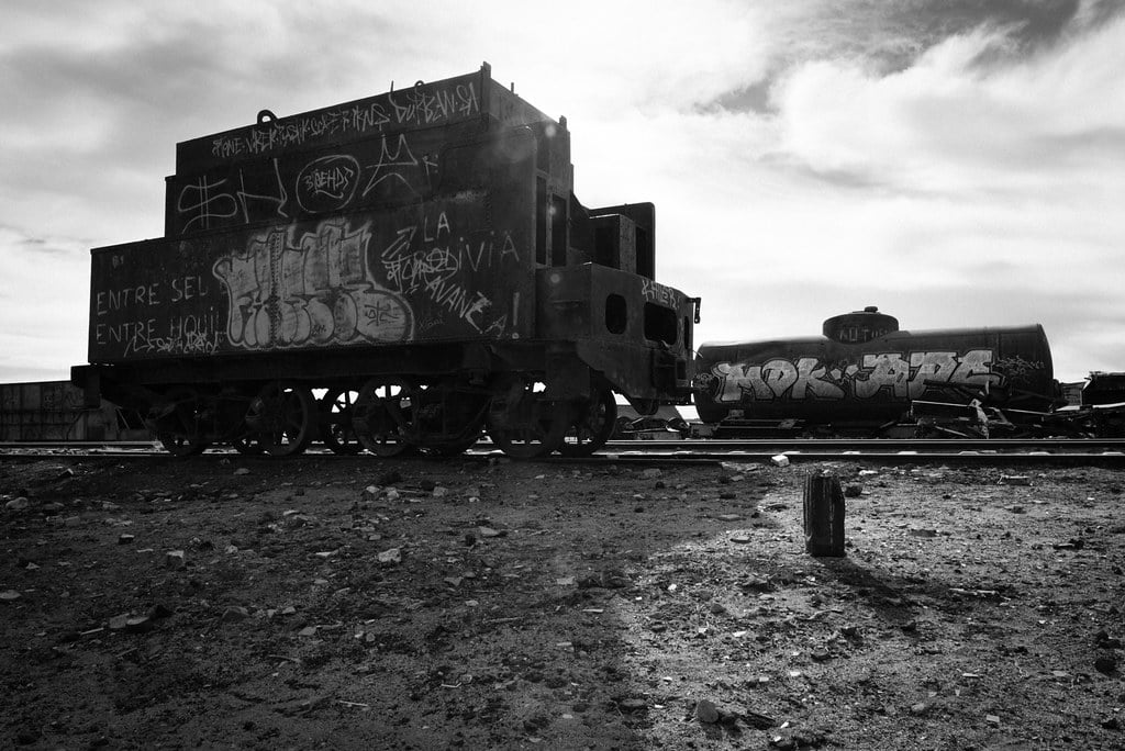 A black-and-white photograph of an abandoned train car in the desert.