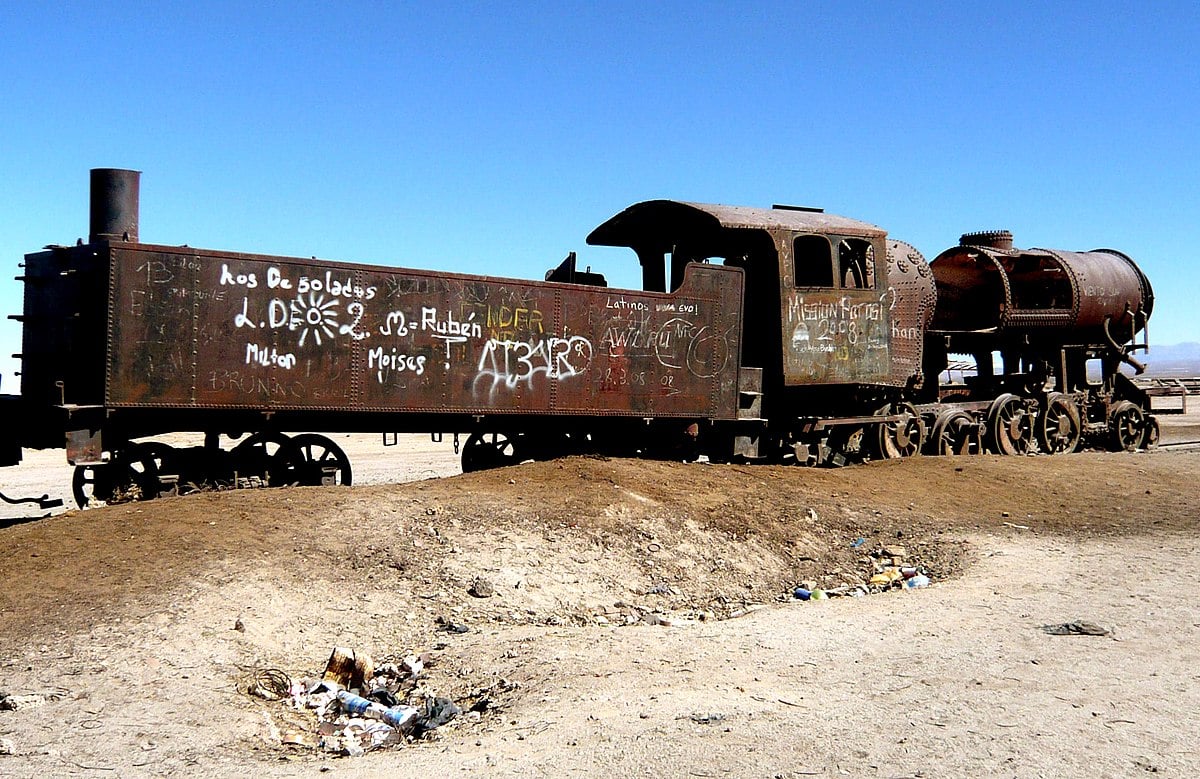An abandoned train car and engine covered with graffiti against a blue sky in the desert.