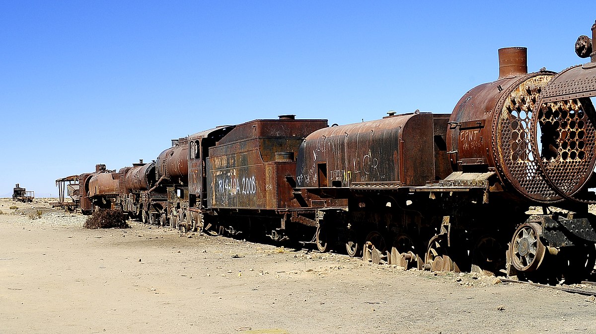 Rusty, abandoned train cars against a blue sky in the desert.