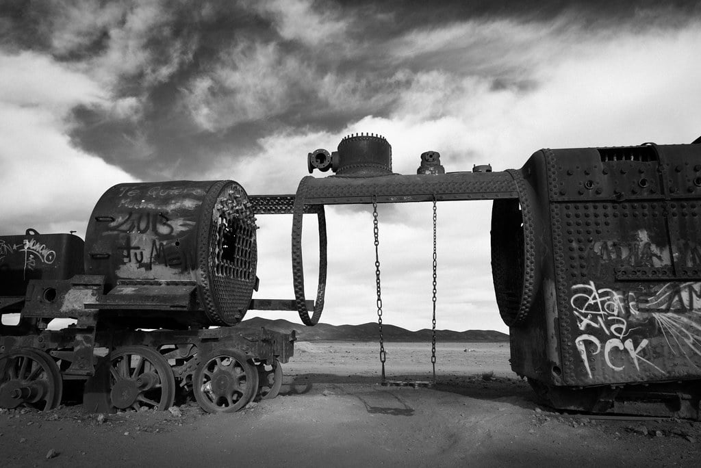 An abandoned shell of a train car in which a swing has been hung. The image is black and white.