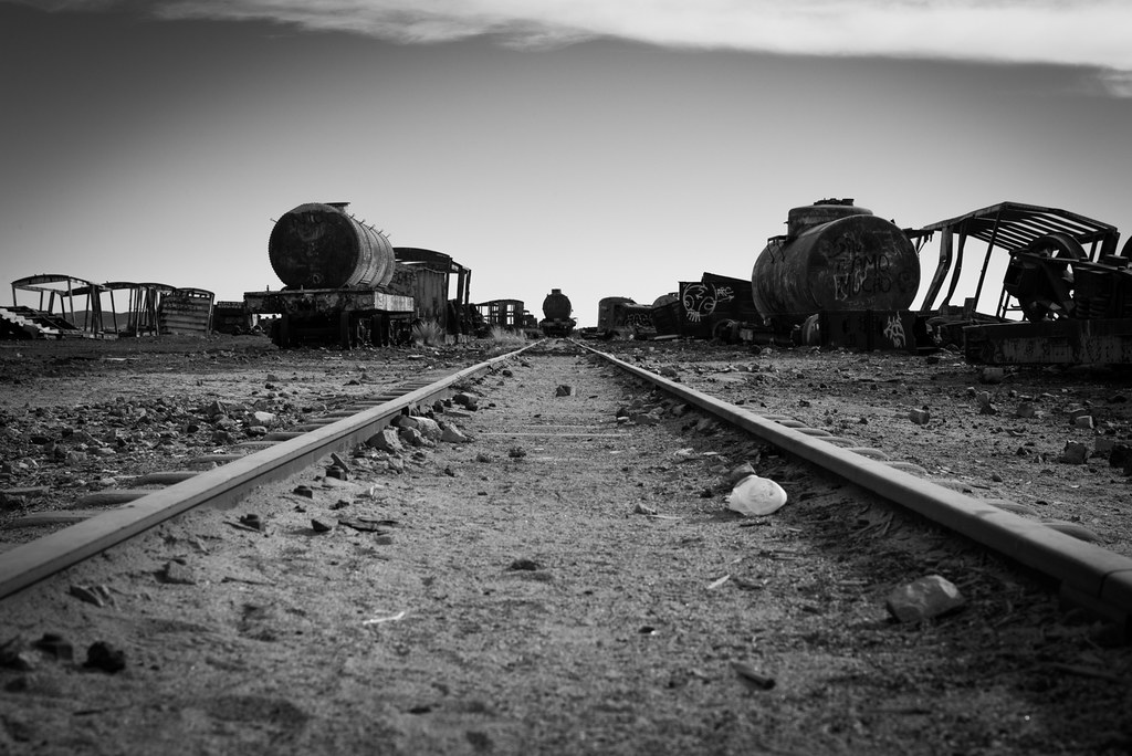 A black-and-white photo of an abandoned train car and tracks.