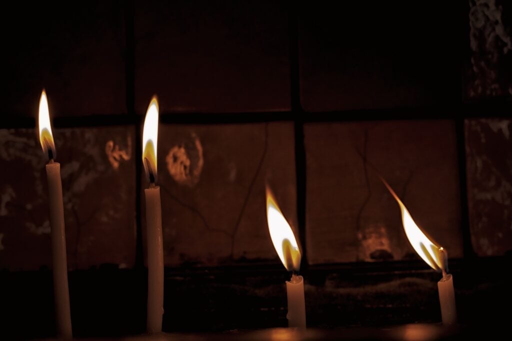 Four tall, skinny candles burning in a dark room.